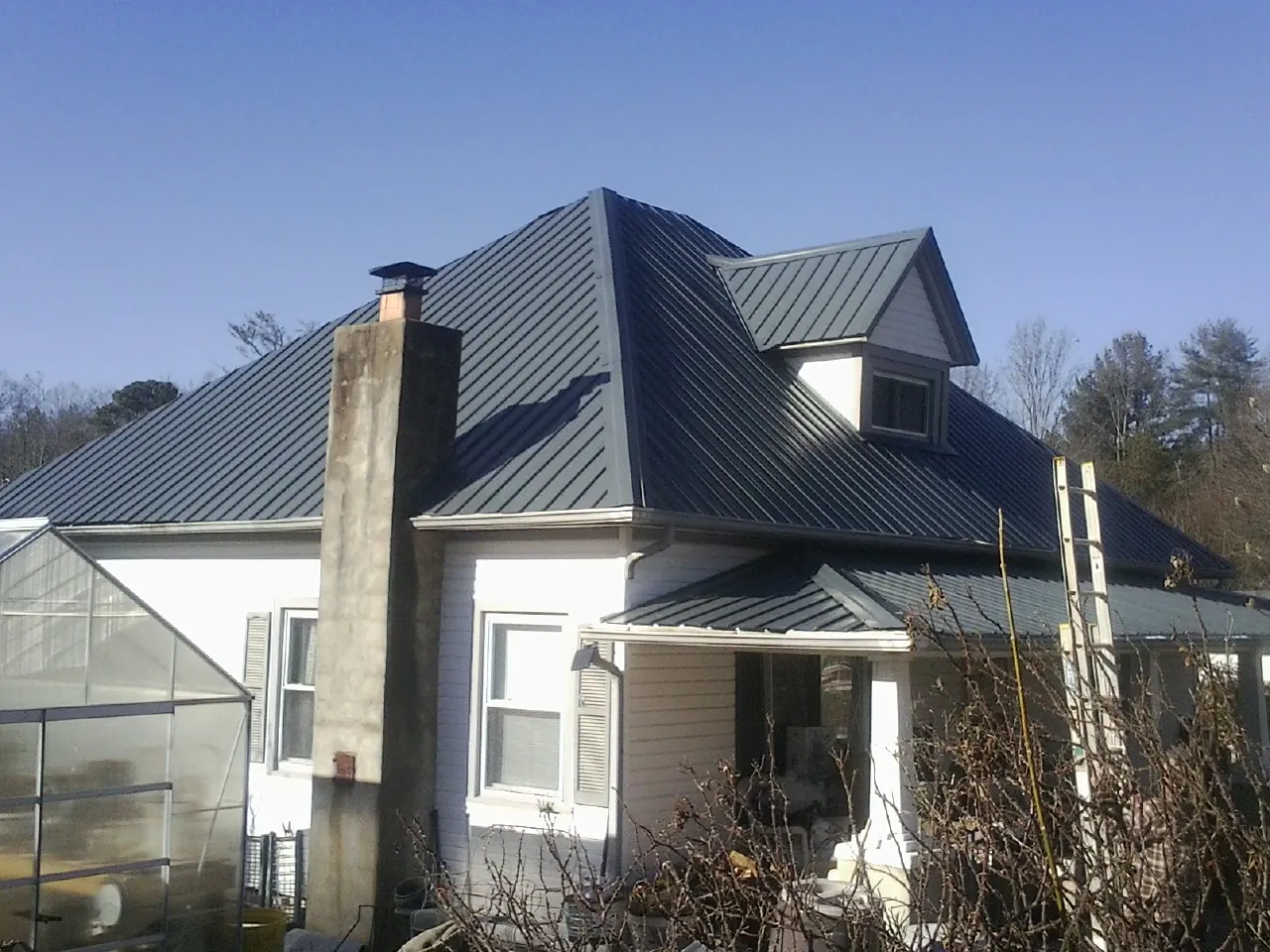 Dark blue standing seam metal roof on a white farmhouse with dormer — Slate & Tile Roof Repair by Roofing Brothers in Sinclair