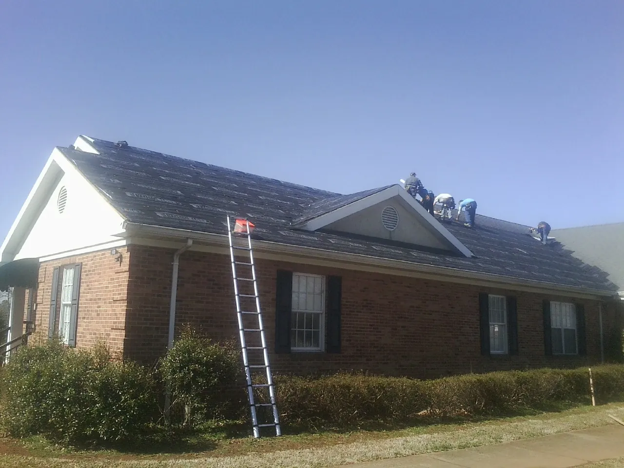 Crew tearing shingles off a brick ranch roof with a ladder set — Emergency Roof Repair work by our crew in Sinclair