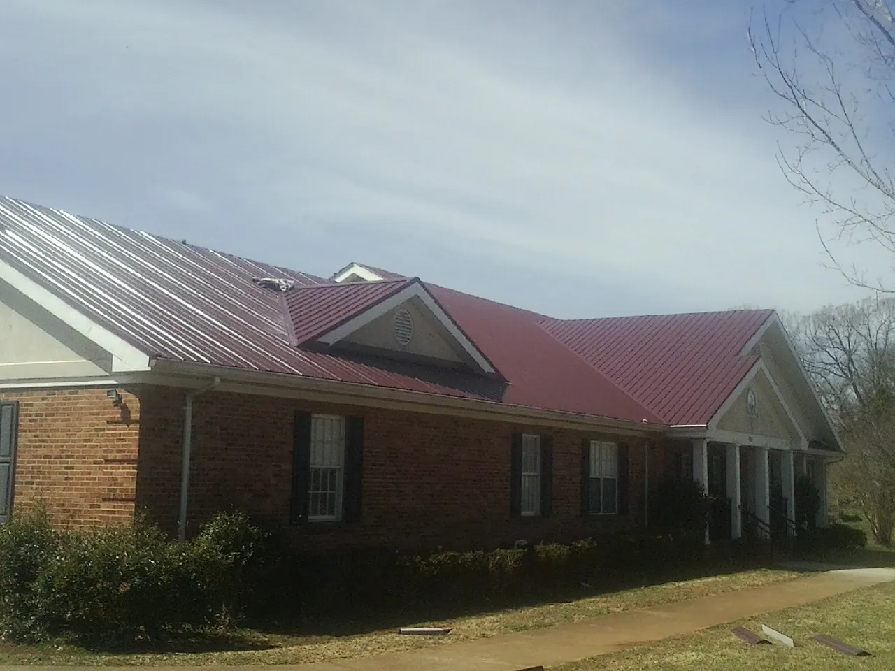 Red metal roof with gabled entries on a long brick building, from a Hail Damage Roof Repair job in Sinclair