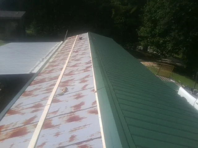 Old rusted panels beside newly installed green metal roofing — Wind Damage Roof Repair by Roofing Brothers in Sinclair