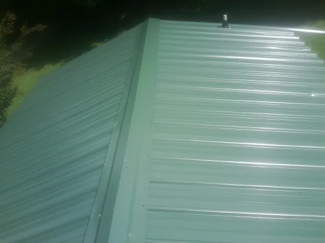 New green metal panels meeting at the ridge of a roof — Flat Roof Repair work by our crew in Sinclair