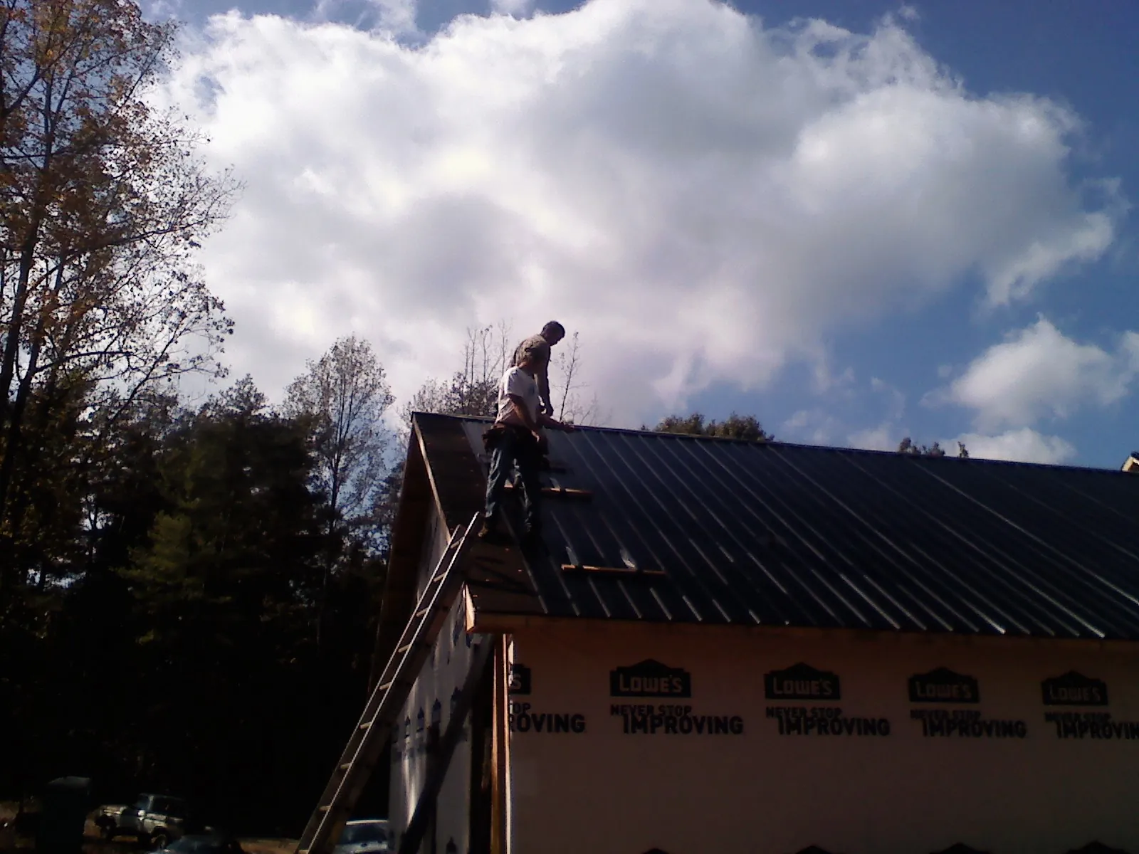 Roofer fastening dark metal panels high against a cloudy sky, from a Roof Inspection job in Sinclair